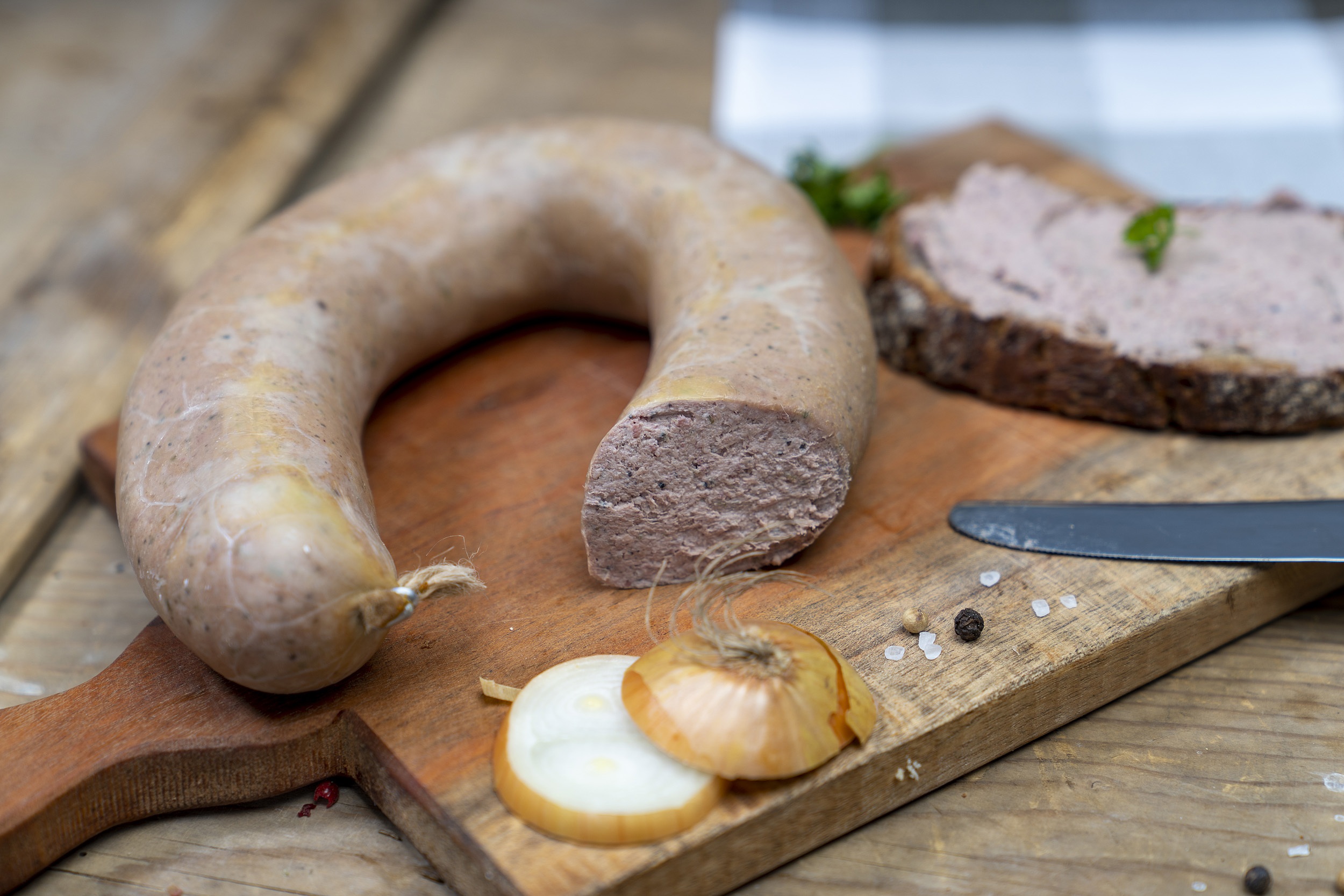Auf einem Brett eine Leberwurst, ein geschmiertes Brot damit und Zwiebeln.
