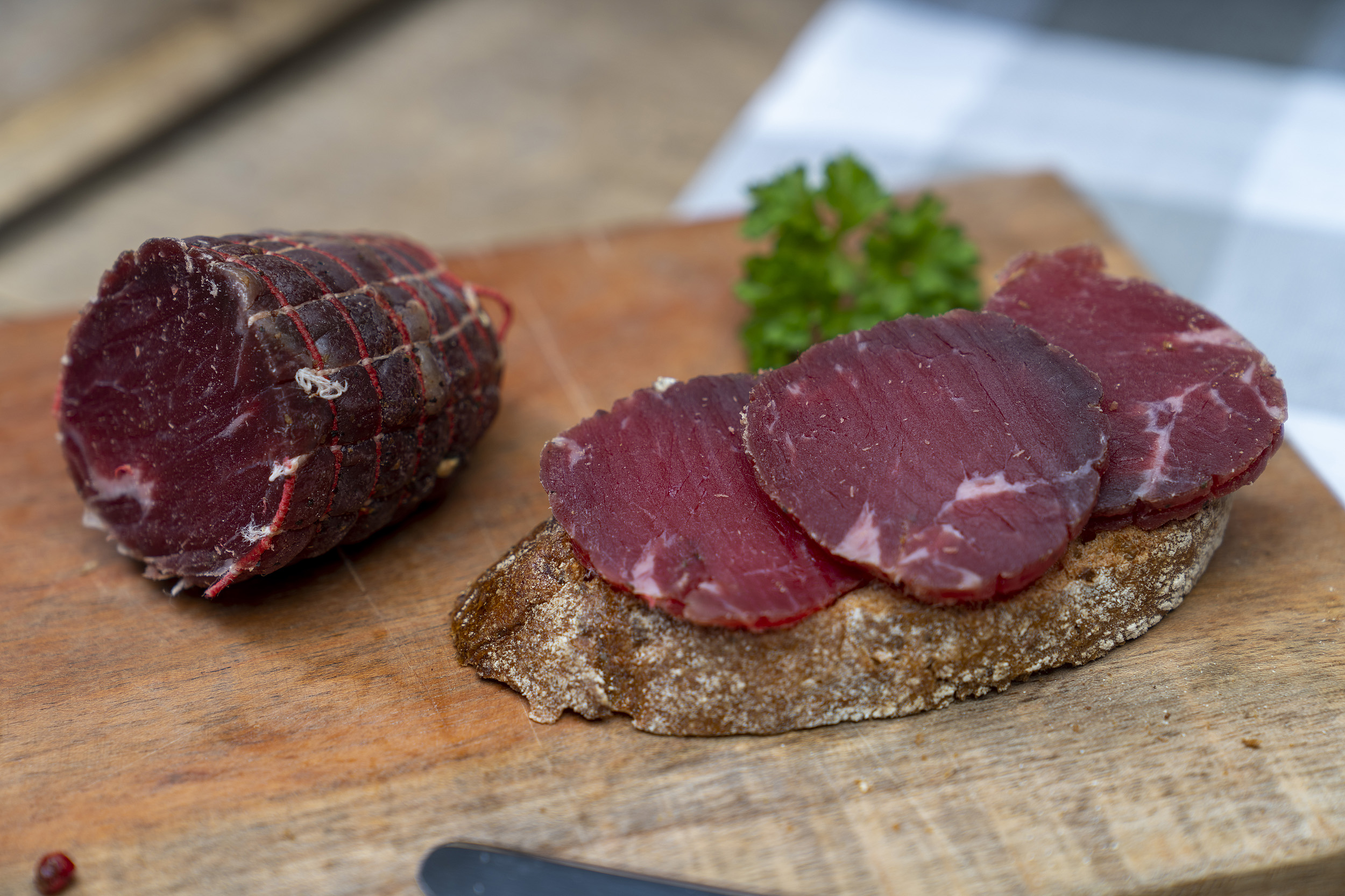 Ein Brot mit Rinderschinken. Auch auf dem Brett das Schinkenstück und Petersilie.
