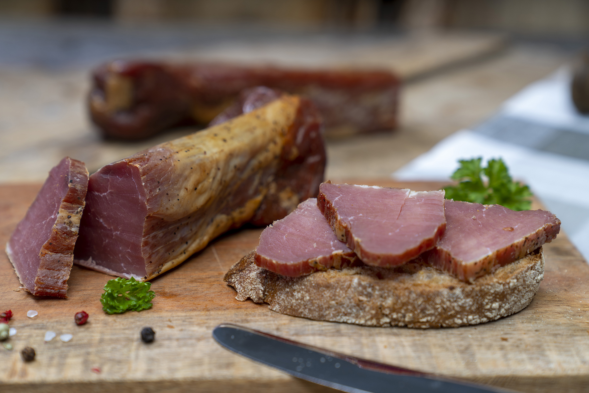 Ein Stück Schinkenfilet der Fleischerei Fessel. Daneben ein Brot mit Schinken. Im Hintergrund ein weiterer Schinken.