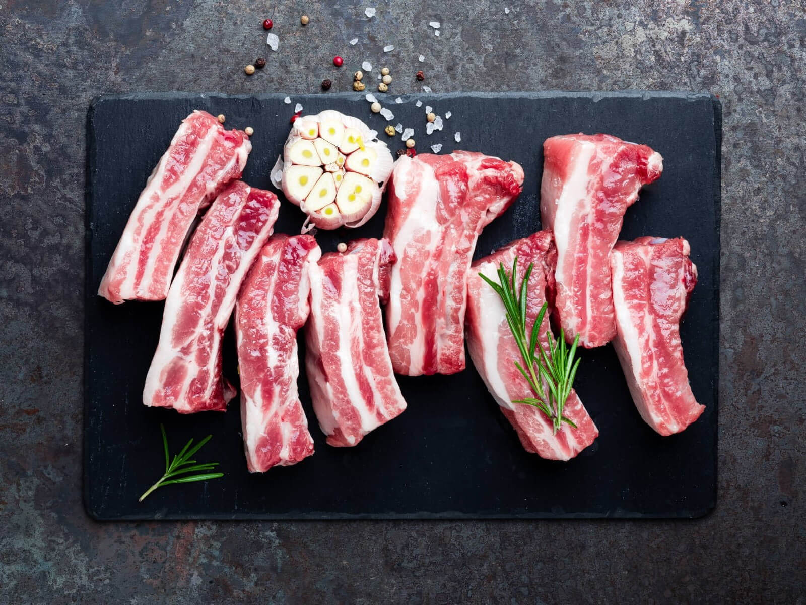 Scheiben Dicke Rippe auf einem dunklen Teller. Darauf Kräuter und Gewürze.