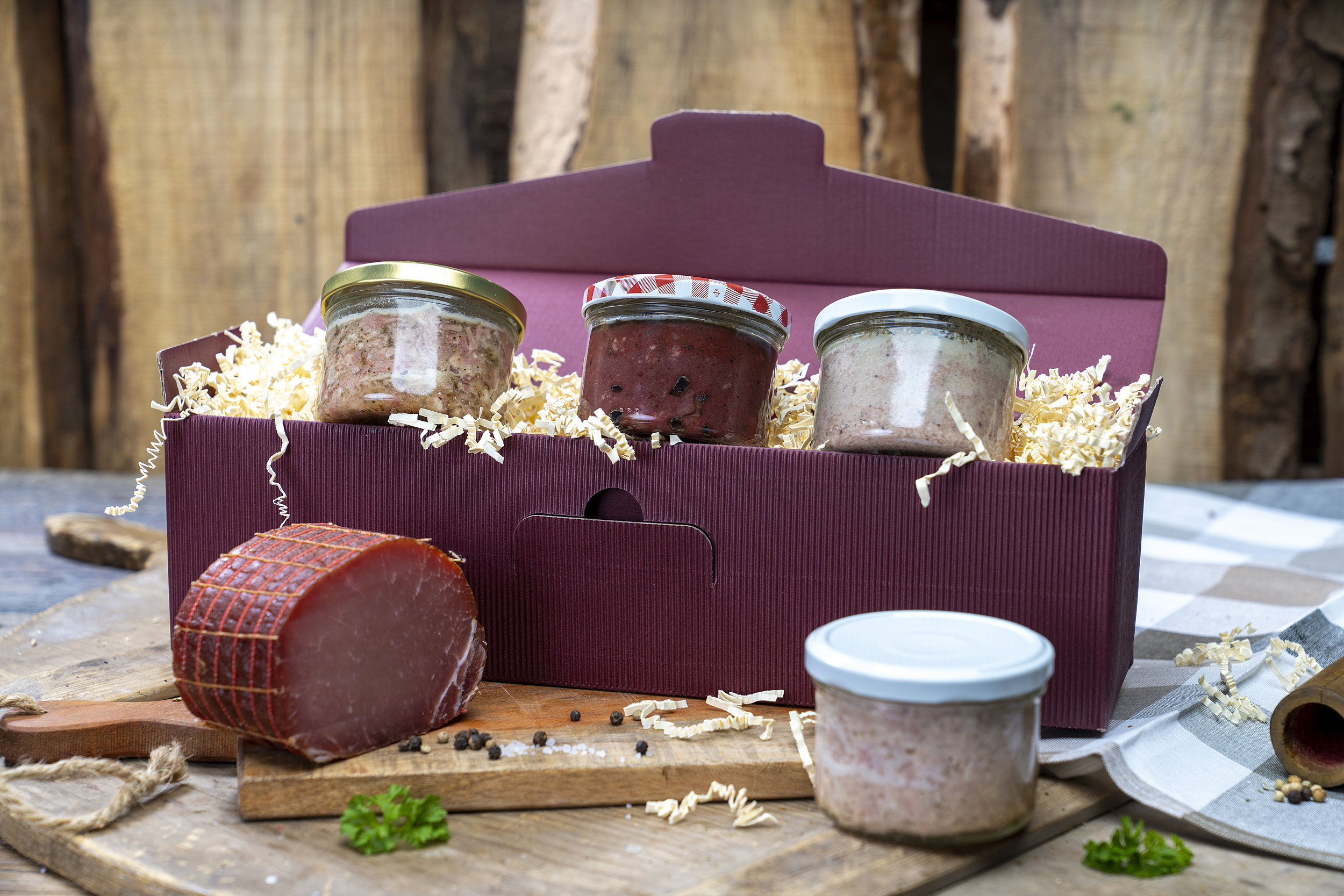 Roter  Geschenkkarton mit vier verschiedenen Konservengläsern und einem Schinken der Fleischerei Fessel.