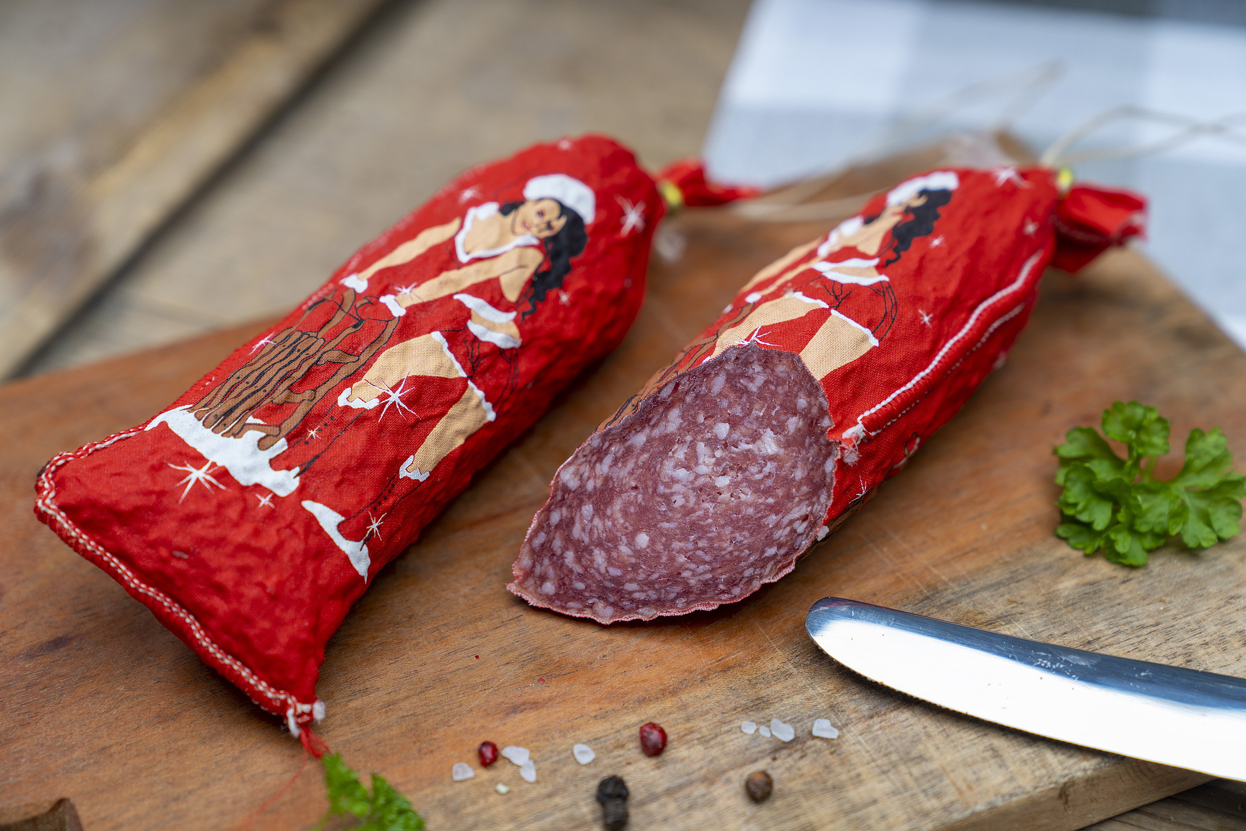 Auf einem Brett eine Salami im weihnachtlichen Look. Daneben eine angeschnittene Salami und Gewürze.