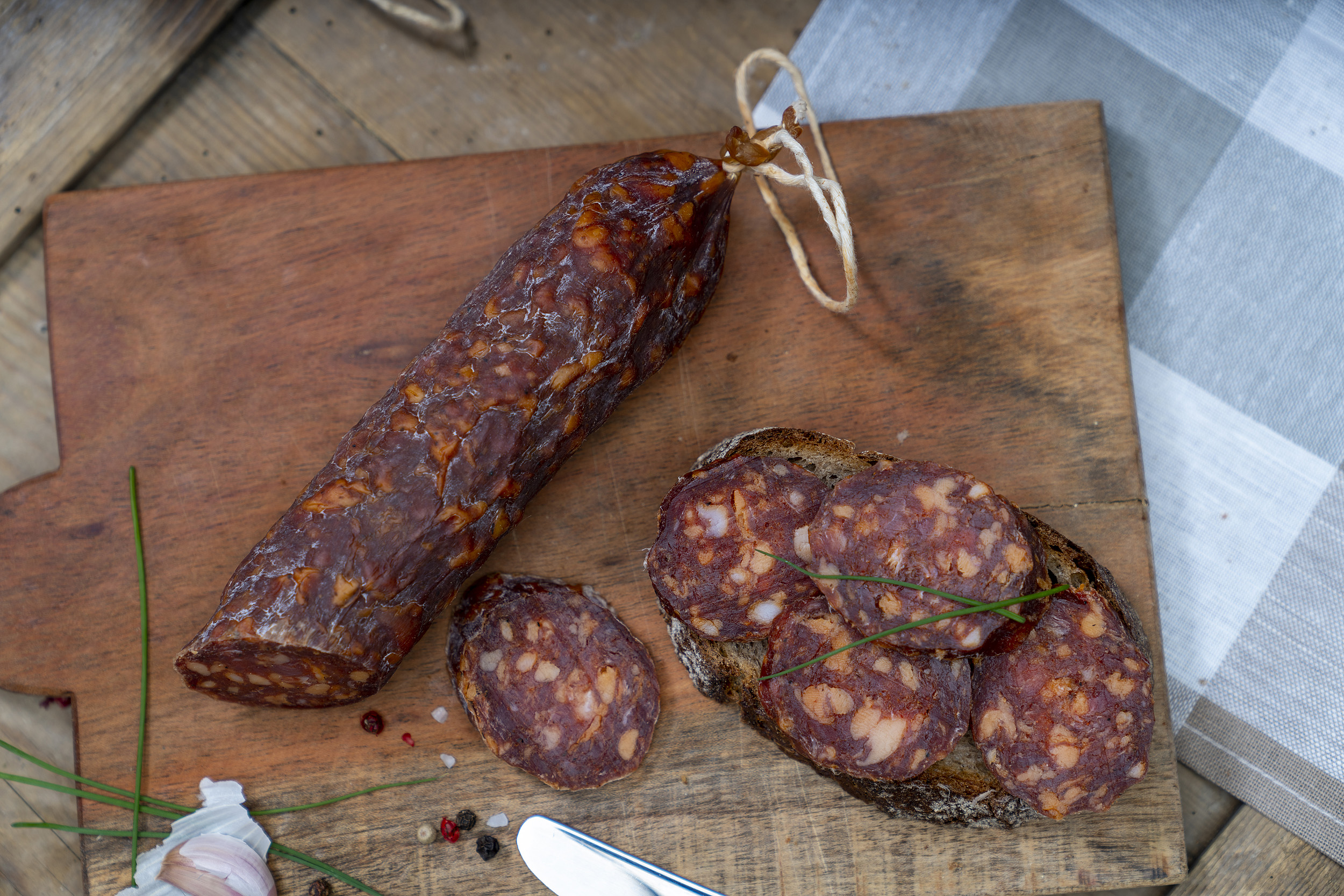 Angeschnittene Ungarische Salami auf einem Brett. Daneben eine Schnitte mit der Wurst und Gewürze.