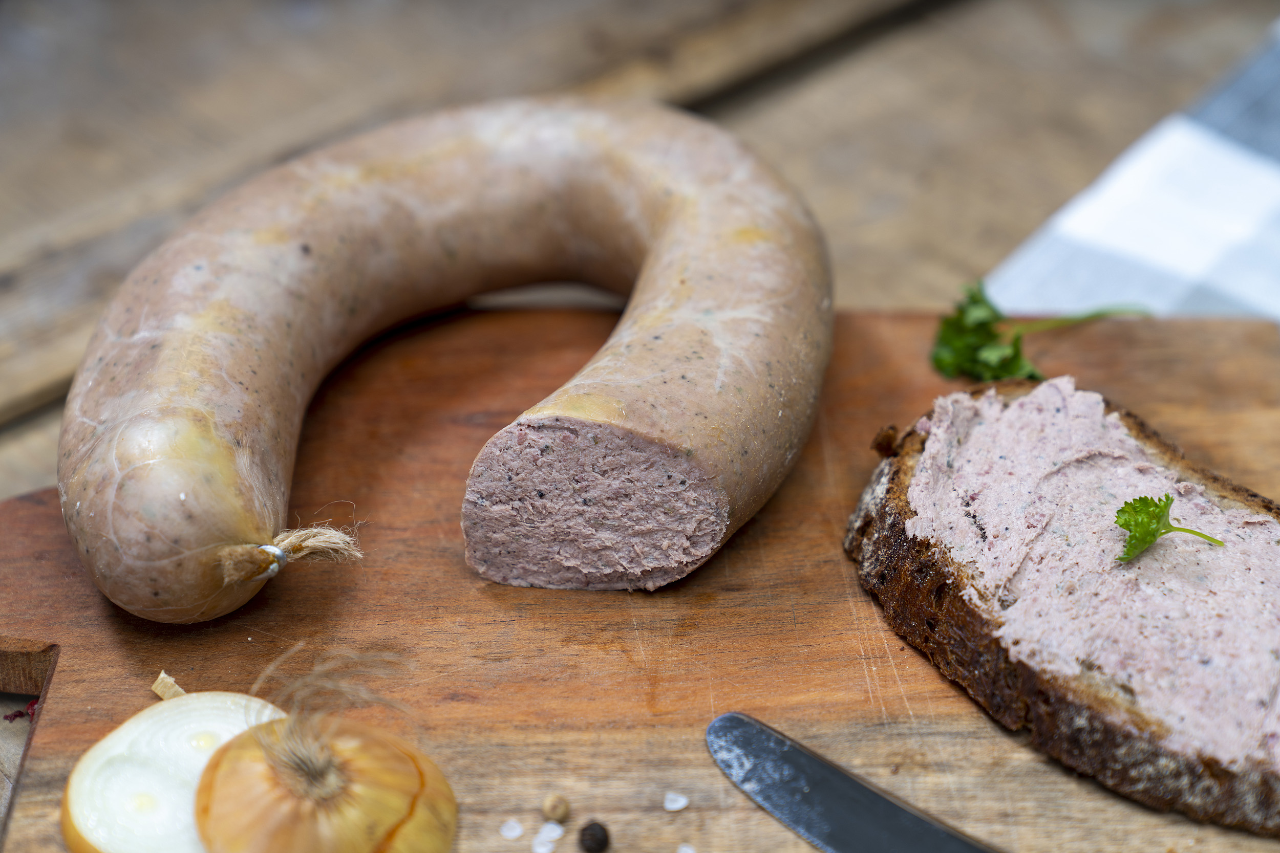 Auf einem Brett eine Leberwurst, ein geschmiertes Brot damit und Zwiebeln.