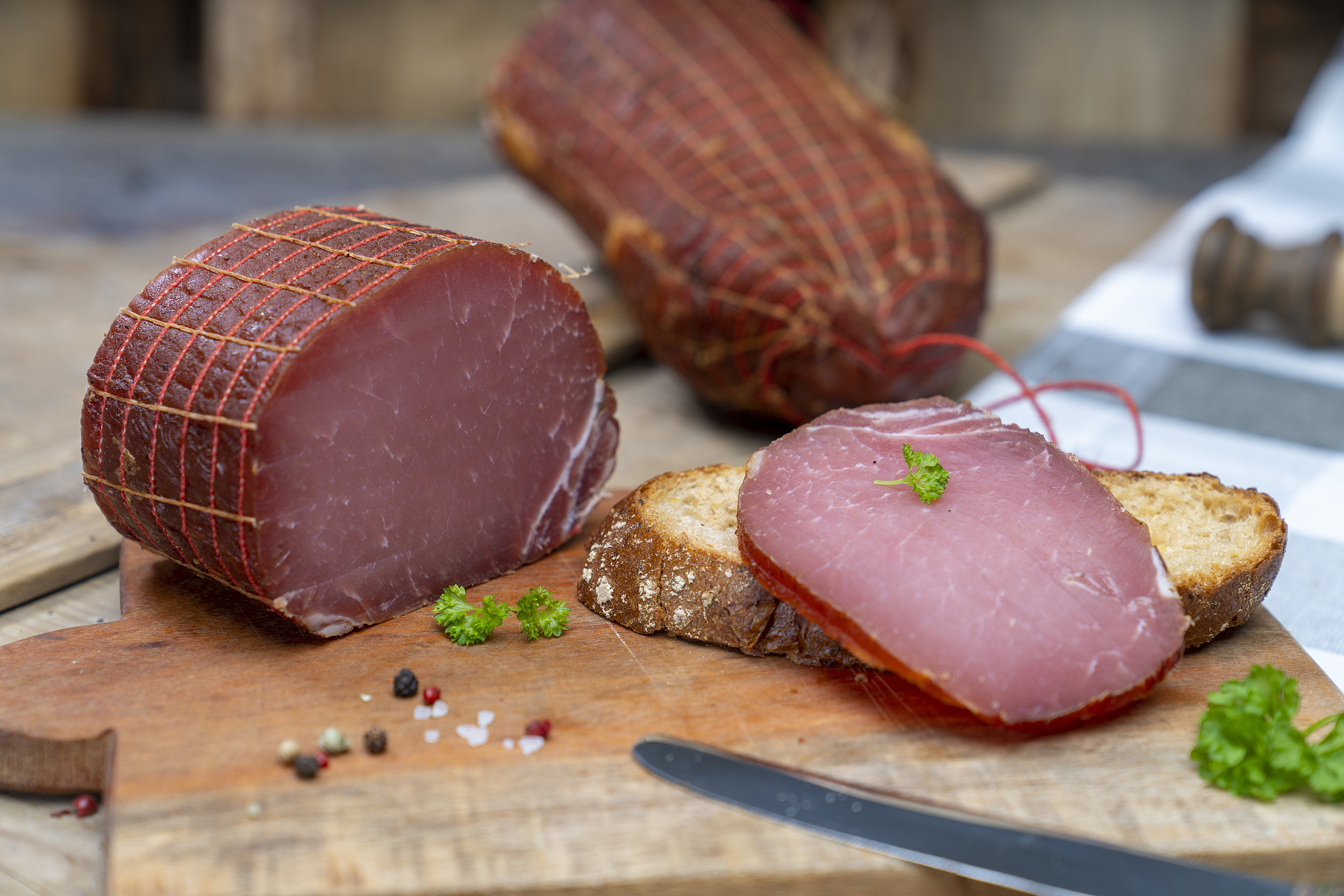 Auf einem Brot eine Scheibe Lachsschinken. Daneben Petersilie und der Schinken. Hinten ein weiterer Schinken.