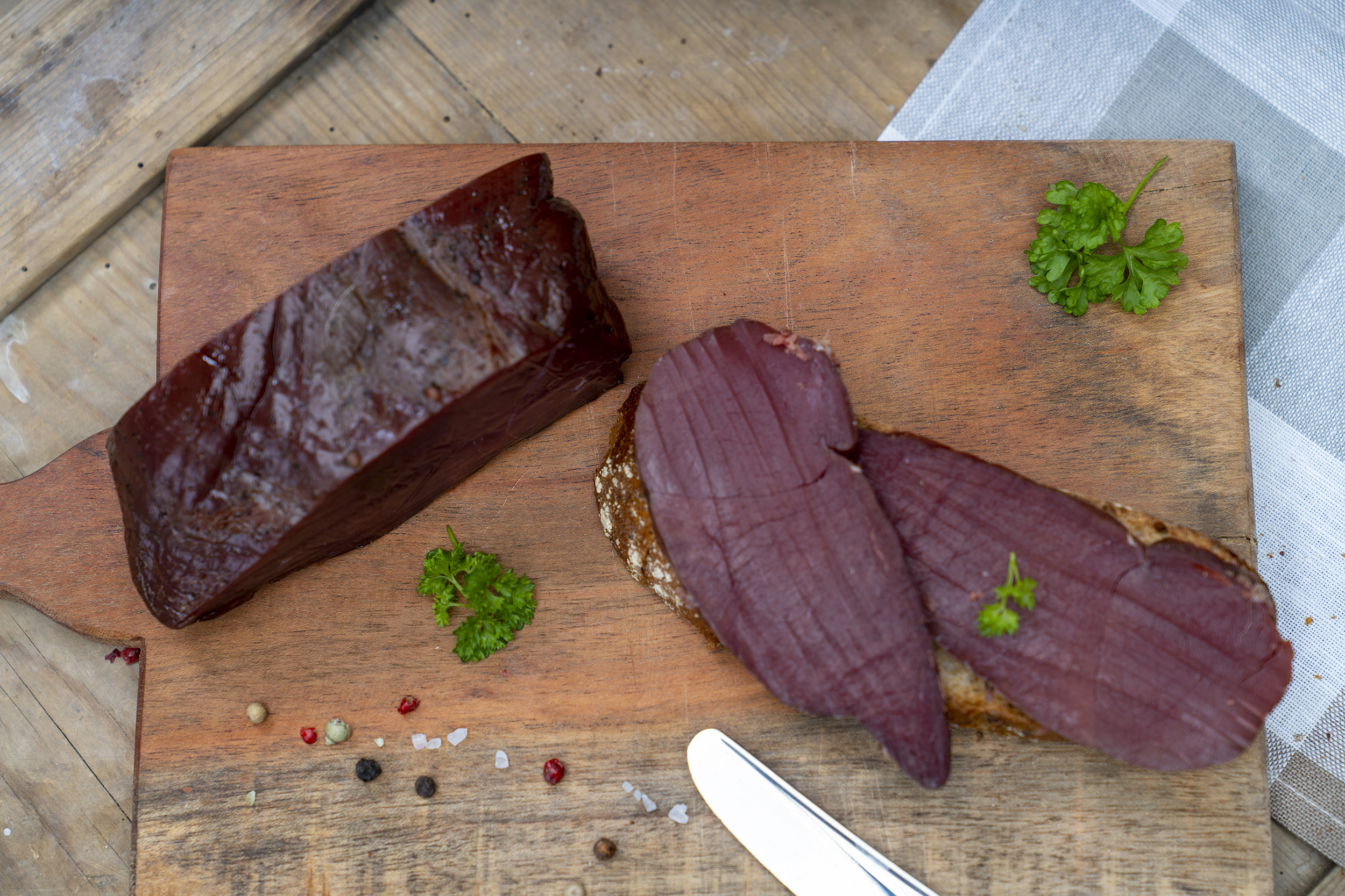 Fessels Wildschinken auf einem Brett. Daneben ein paar Scheiben und Gewürze.