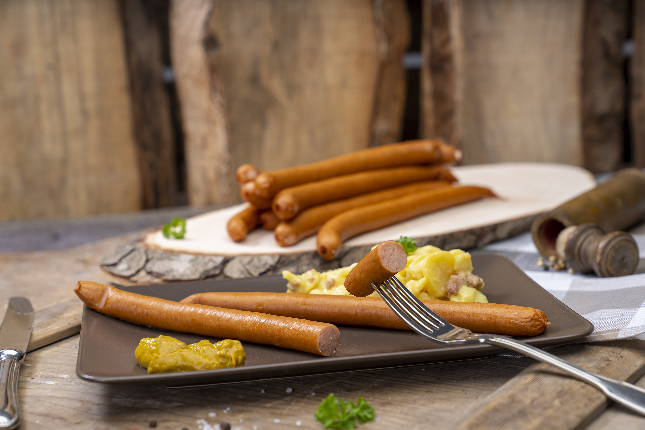 Zwei Wienerwürstchen, Kartoffelsalat und Senf. Hinten weitere Wiener der Fleischerei Fessel.