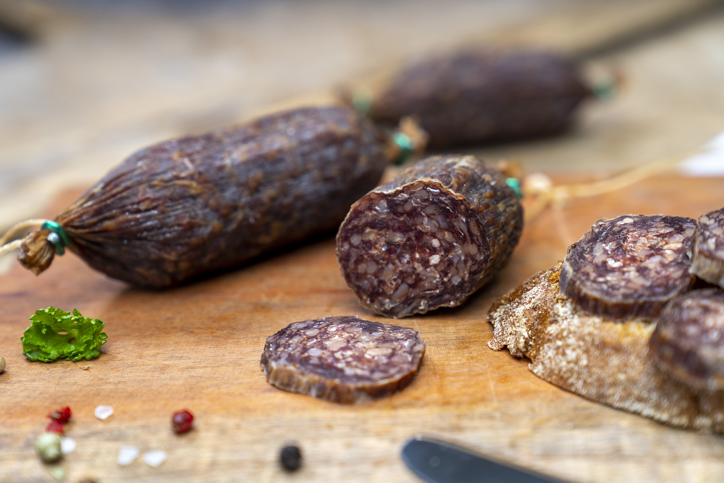 Einige Rindsalamis auf einem Holzbrett. Daneben eine Schnitte mit der Salami.