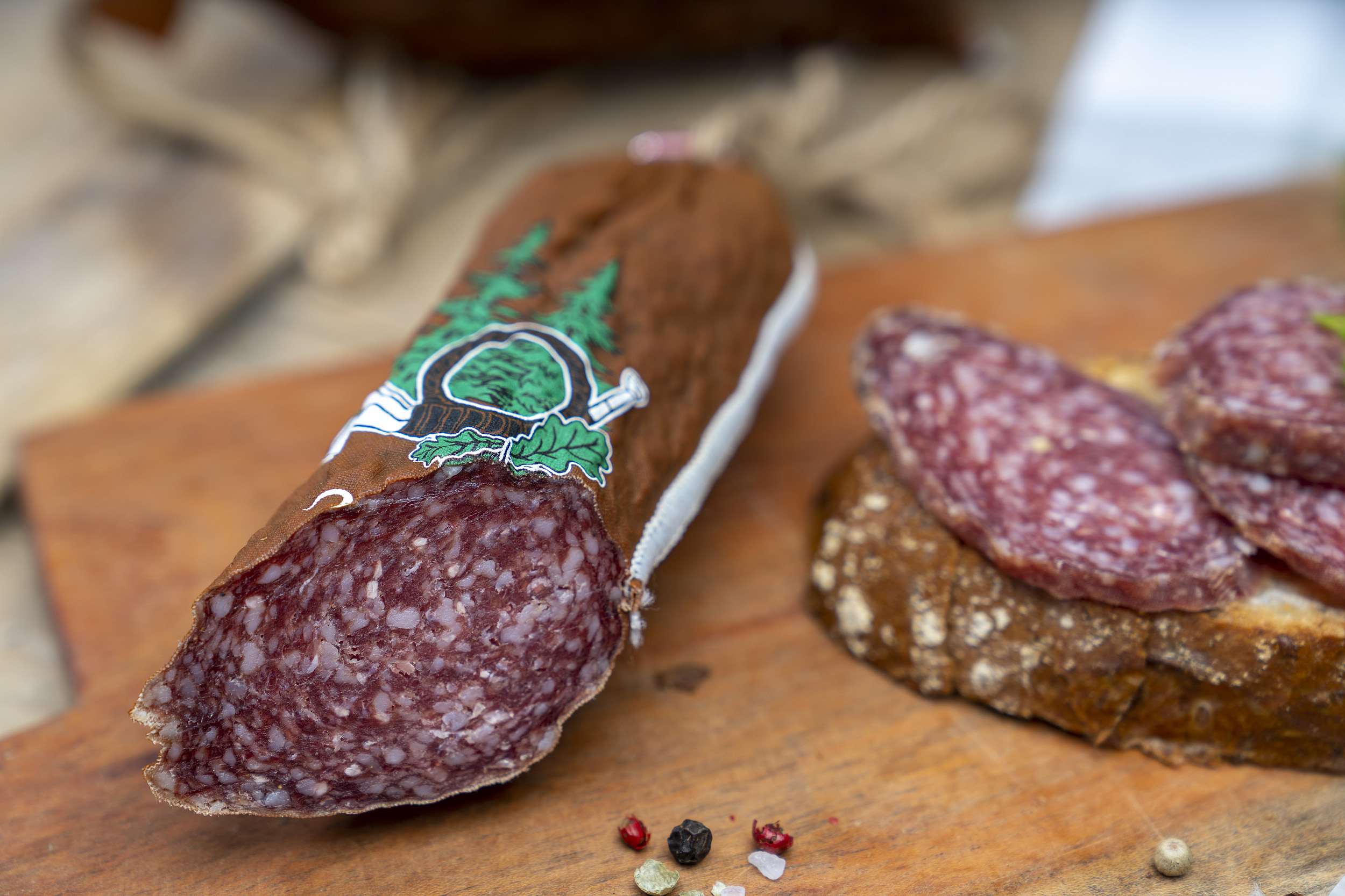 Hirschsalami auf Holzbrett. Daneben eine Schnitte mit Salami und Kräuter.