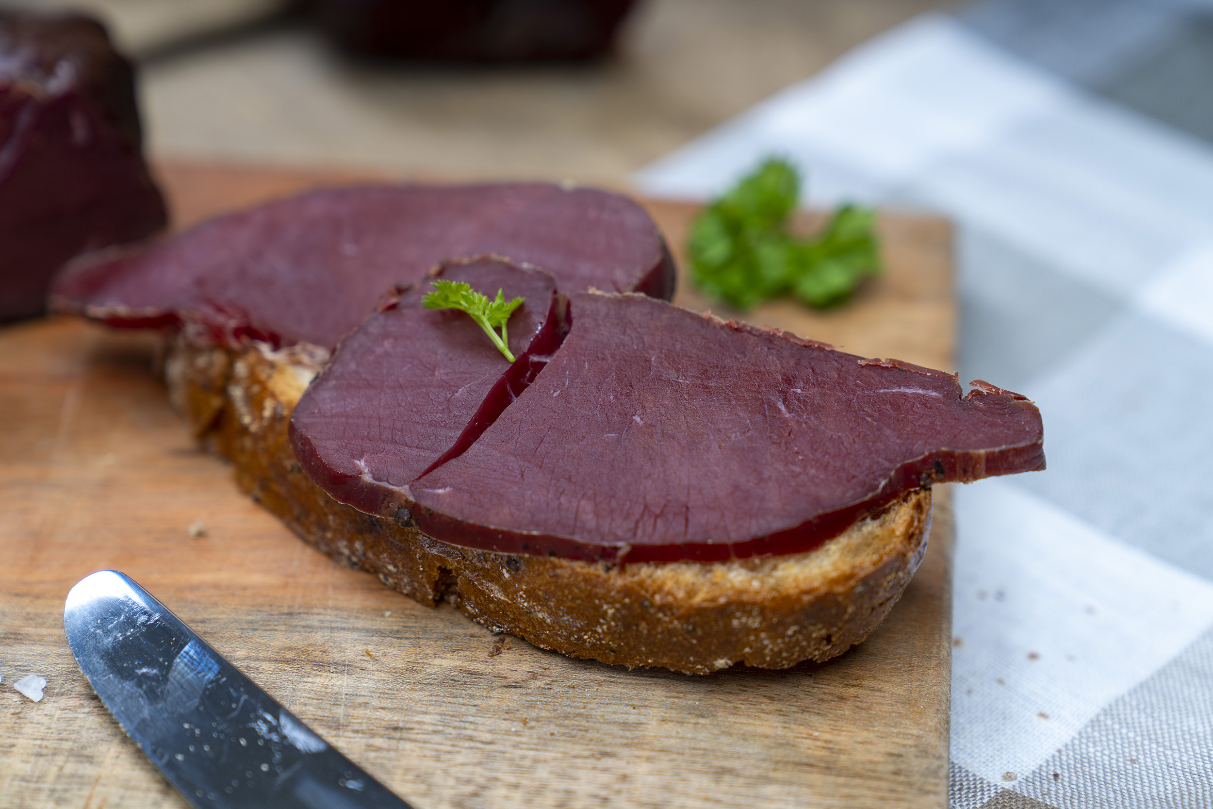 Ein paar Scheiben Wildschinken auf einem Brot. Daneben Gewürze.