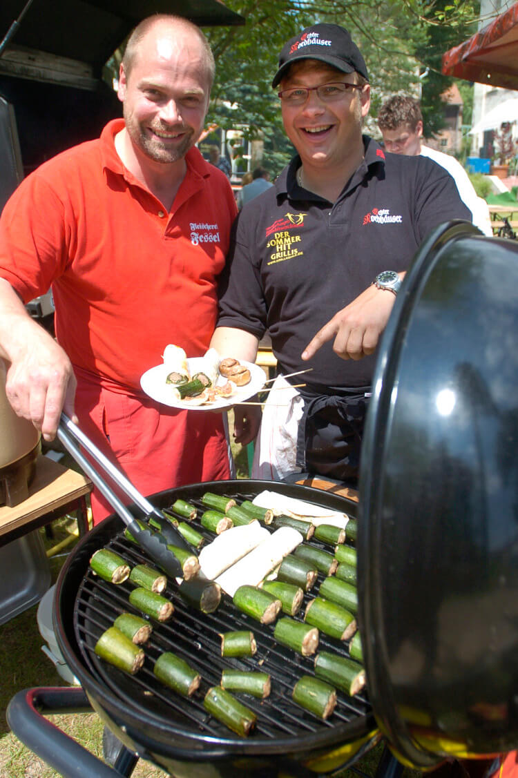 Erwin Fessel und Andreas Rummel stehen gemeinsam am Grill. Beide lachen und die Sonne scheint.