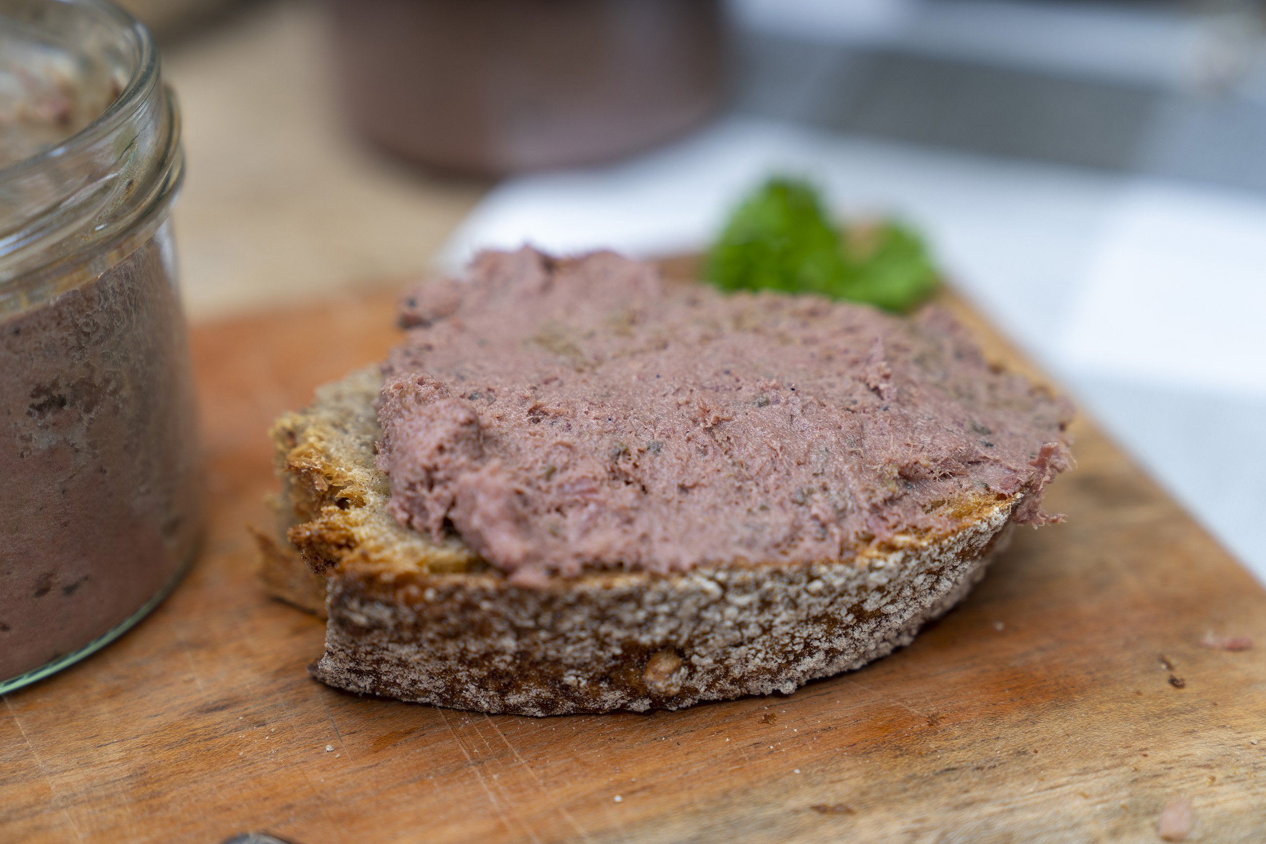 Ein geschmiertes Brot mit Wildleberwurst auf eine Brett. Daneben das Glas.
