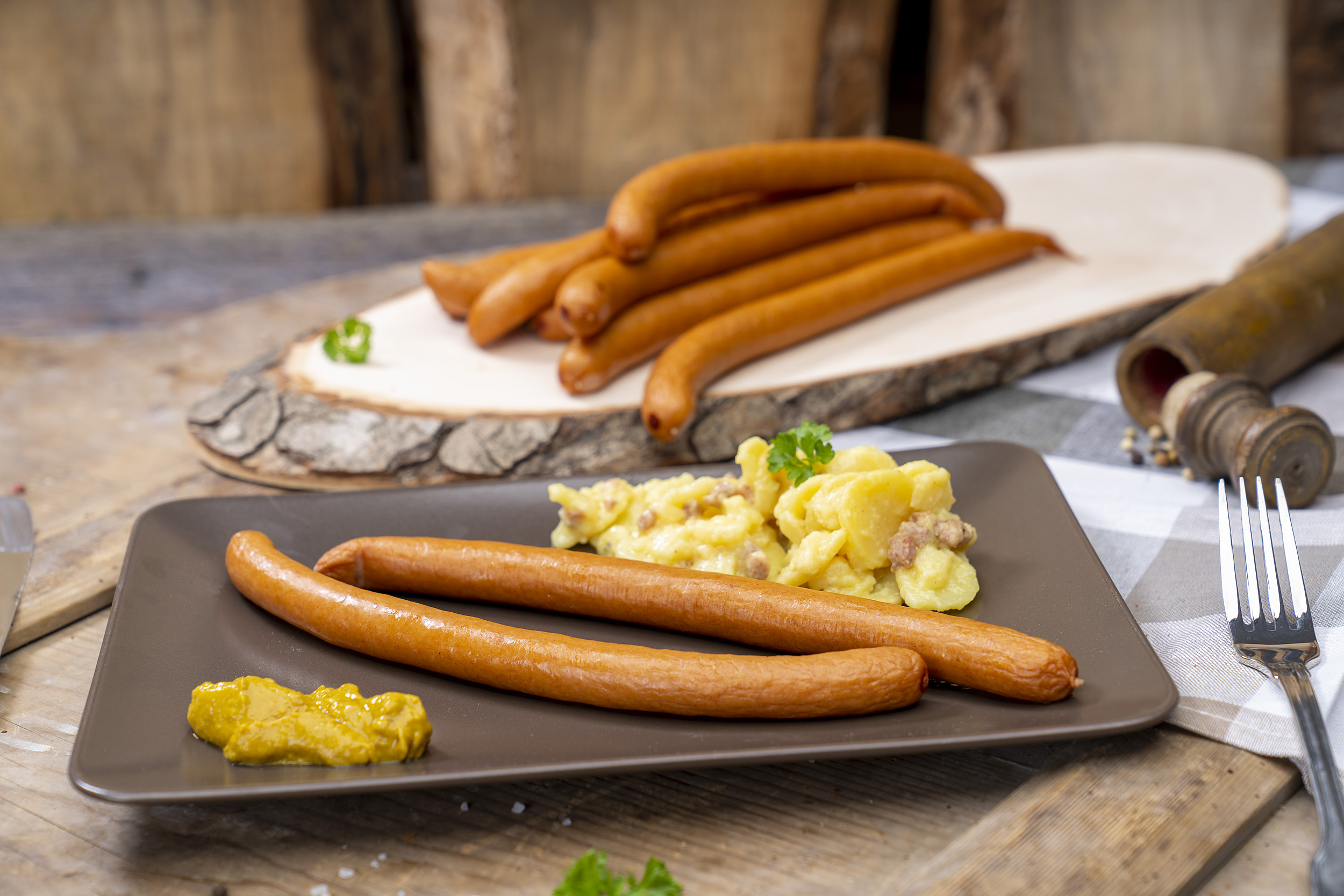 Zwei Wienerwürstchen, Kartoffelsalat und Senf. Hinten weitere Wiener der Fleischerei Fessel.