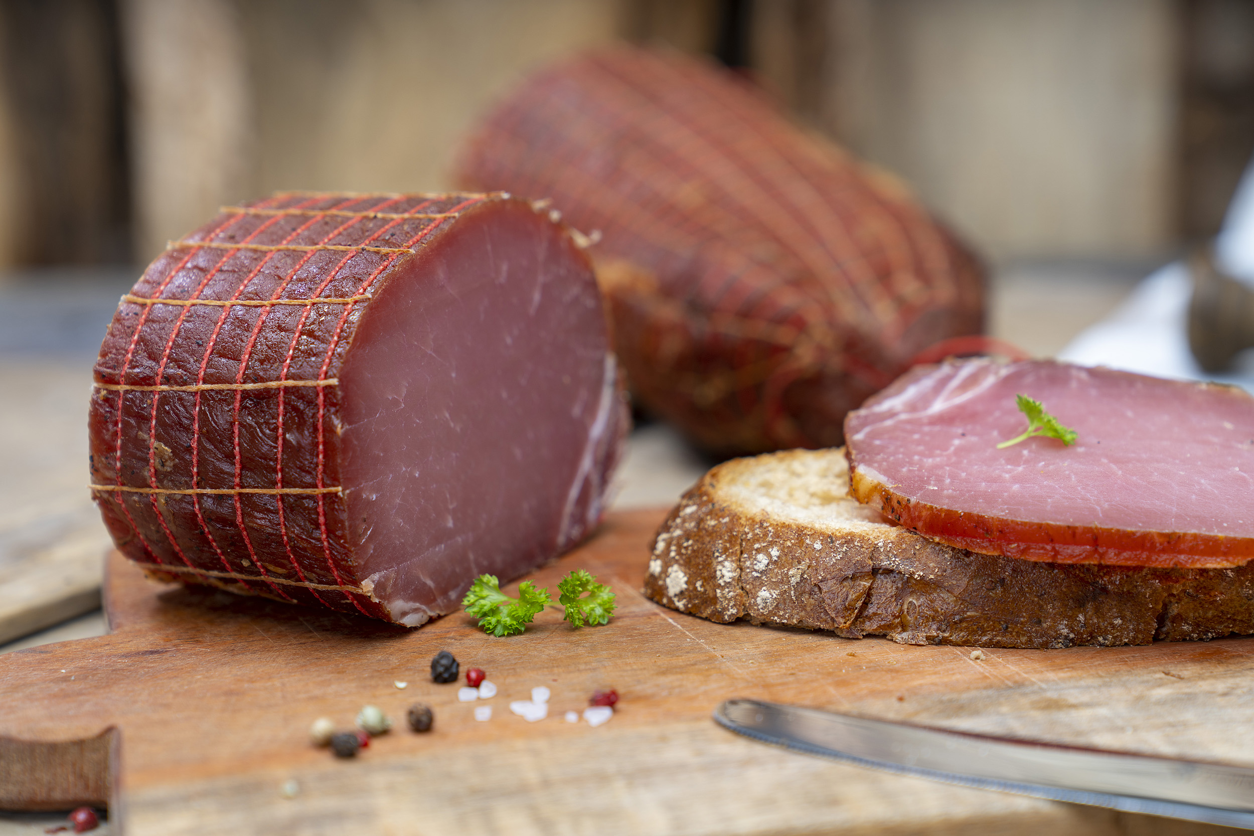 Auf einem Brot eine Scheibe Lachsschinken. Daneben Petersilie und der Schinken. Hinten ein weiterer Schinken.