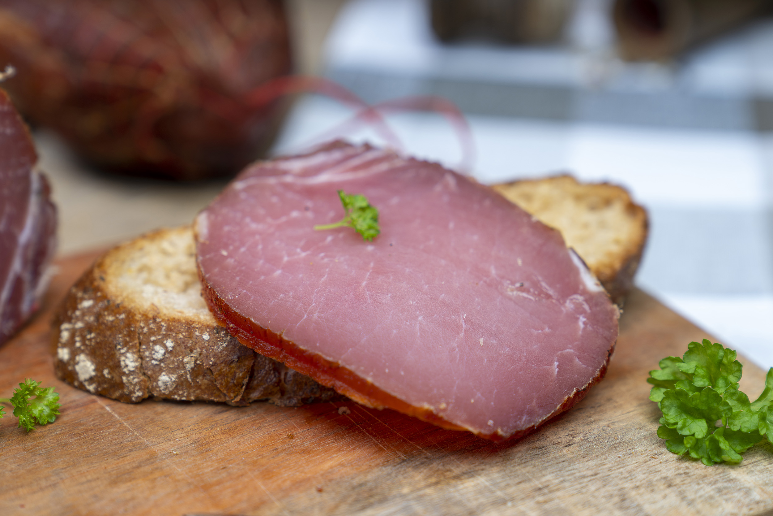Auf einem Brot eine Scheibe Lachsschinken. Daneben Petersilie und der Schinken.