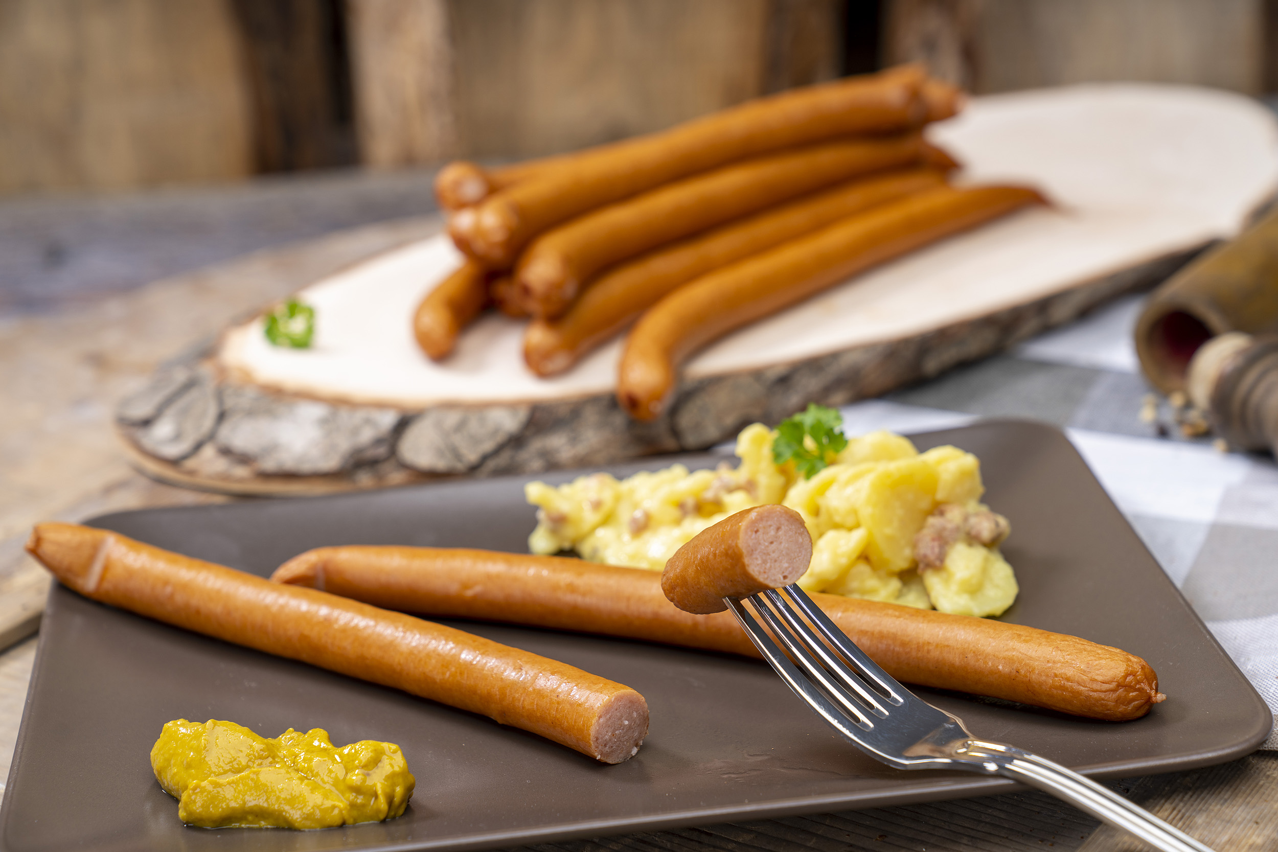 Zwei Wienerwürstchen, Kartoffelsalat und Senf. Hinten weitere Wiener der Fleischerei Fessel.