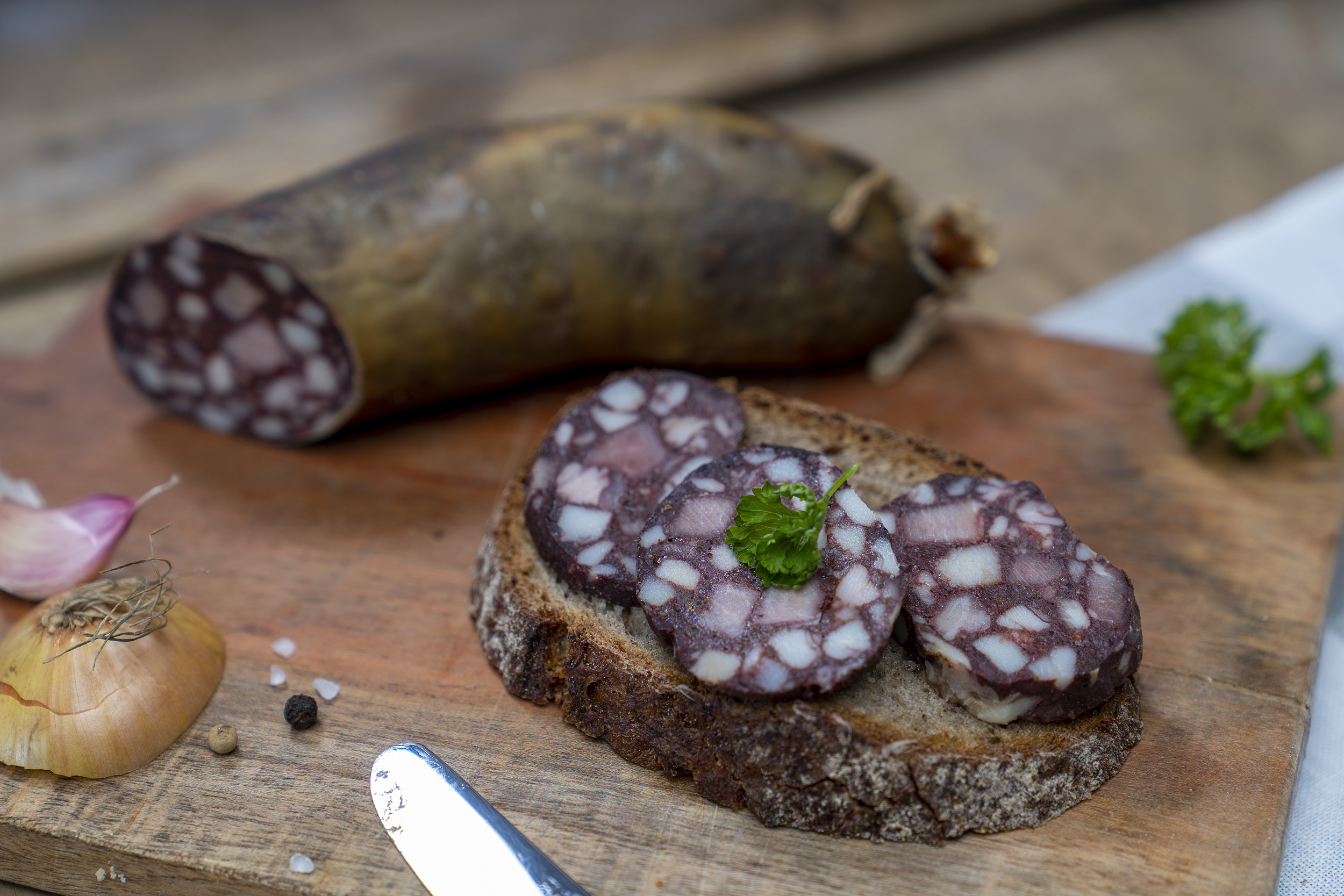Eine Scheibe Brot mit Rotwurst Scheiben. Auf dem Brett Kräuter, Zwiebeln und die Wurst.