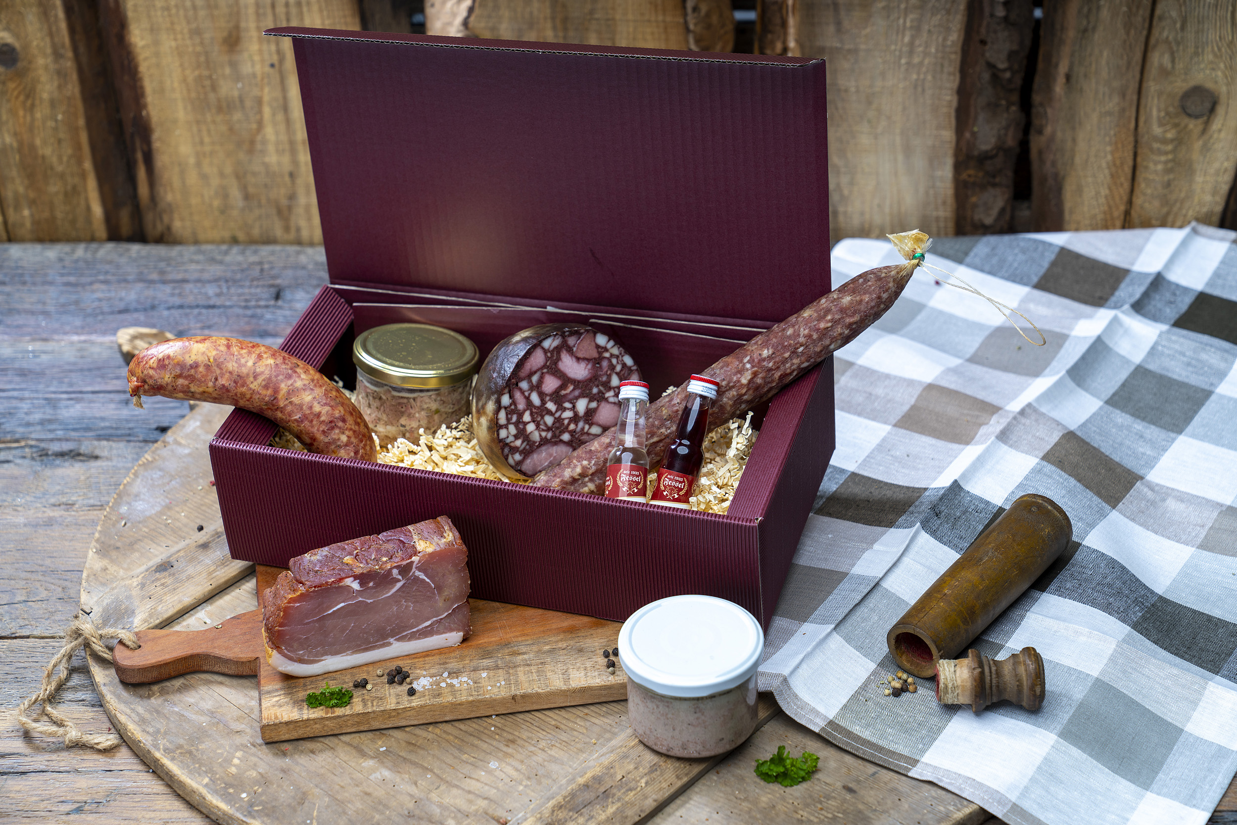 Roter Geschenkkarton mit Würsten und Gläsern auf einem Tisch.