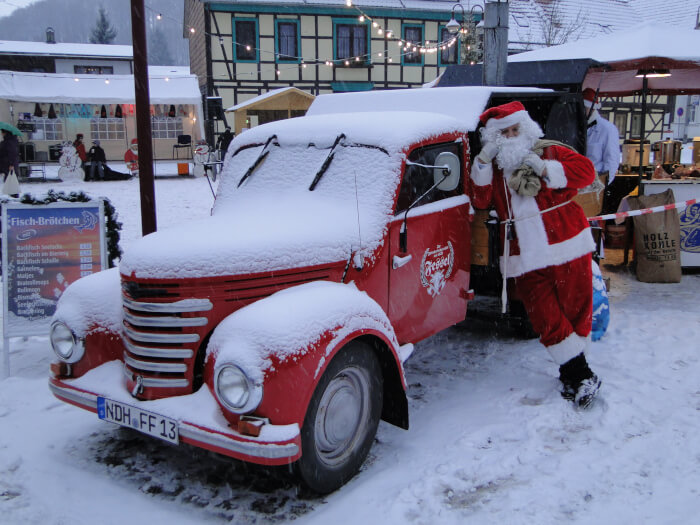Der neue Framo ganz in rot. Er steht auf dem Weihnachtsmarkt in Ilfeld und ist ganz zu geschneit. Daran lehnt der Weihnachtsmann. Im Hintergrund Lichter und Häuser.