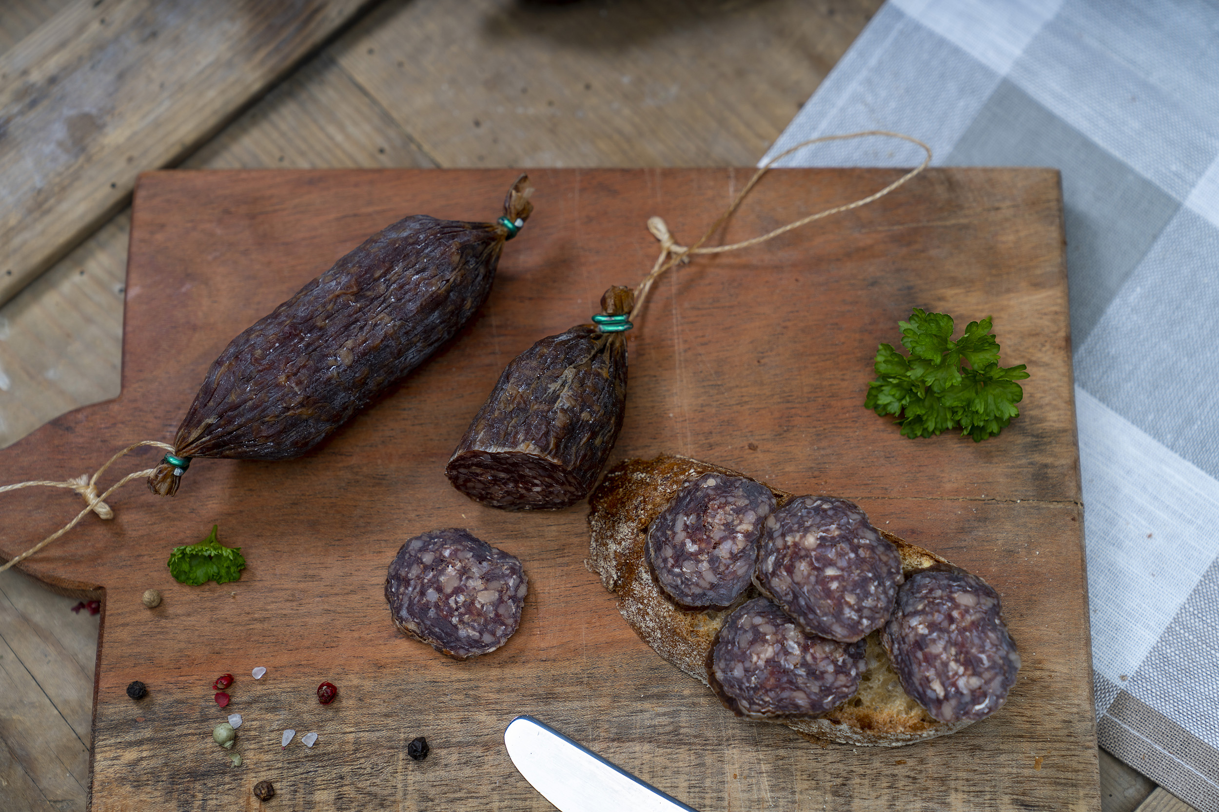 Einige Rindsalamis auf einem Holzbrett. Daneben eine Schnitte mit der Salami.