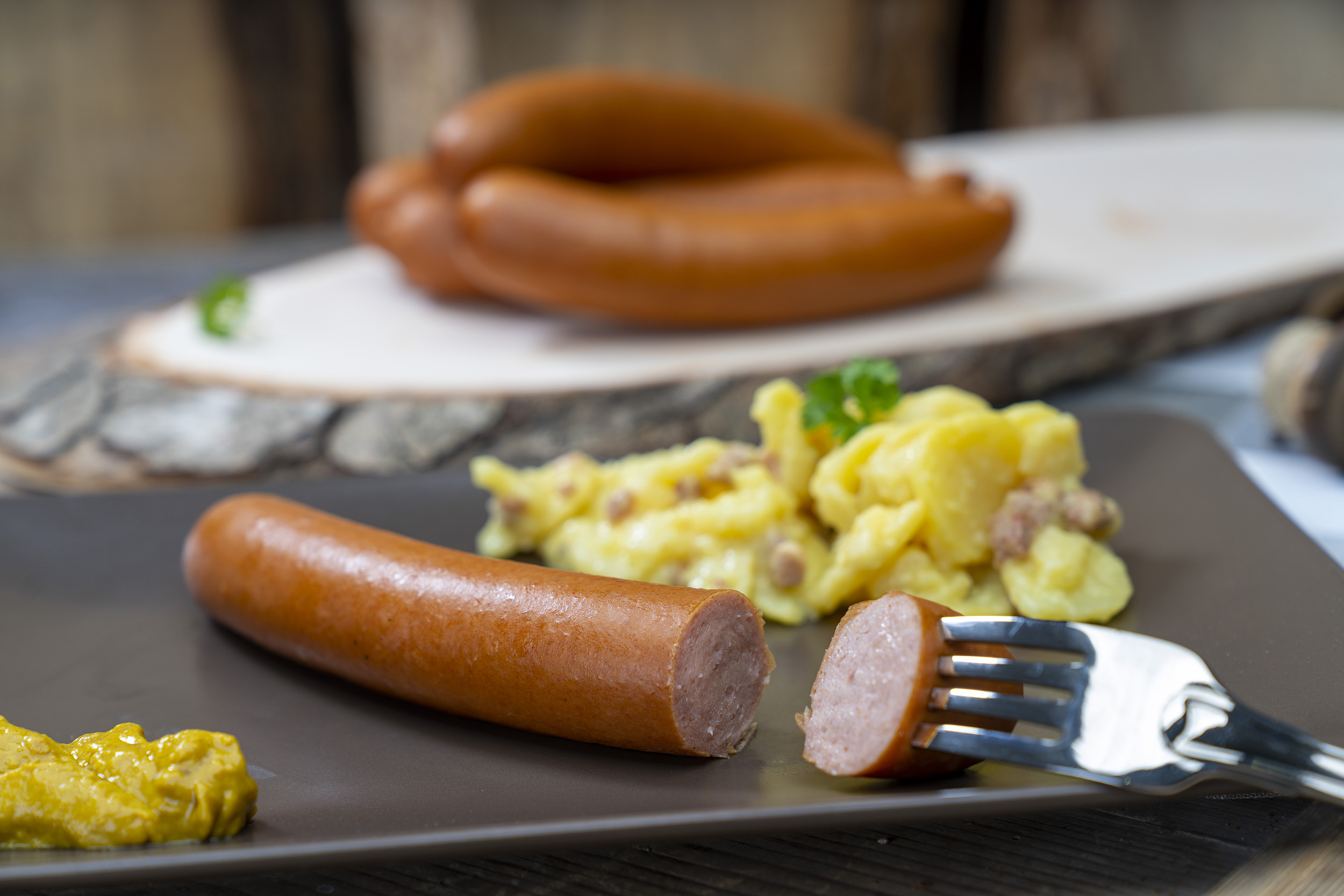 Bockwurst auf einem Teller mit Senf und Kartoffelsalat. Hinten mehr Bockwürsten der Fleischerei Fessel.