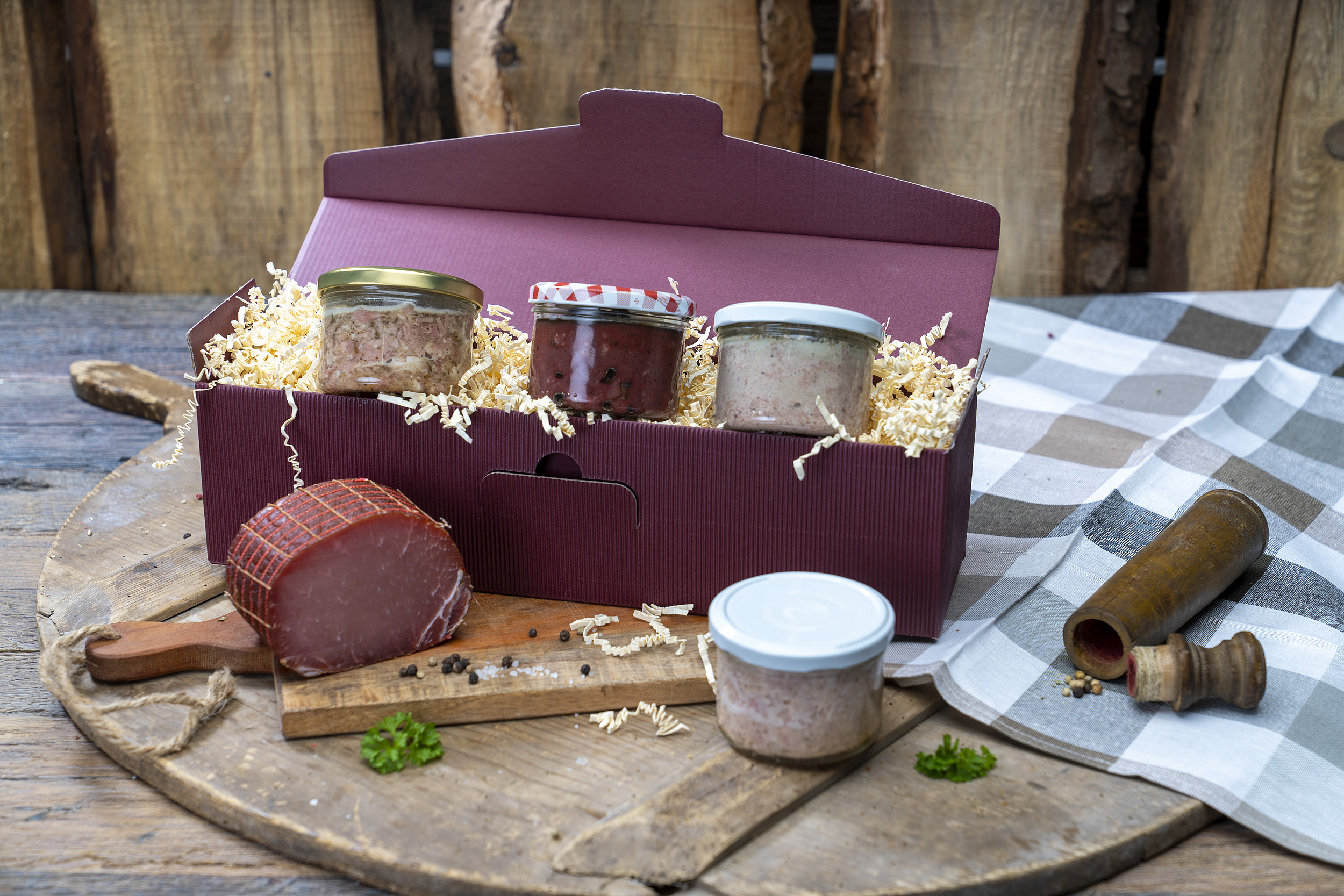 Roter  Geschenkkarton mit vier verschiedenen Konservengläsern und einem Schinken der Fleischerei Fessel.