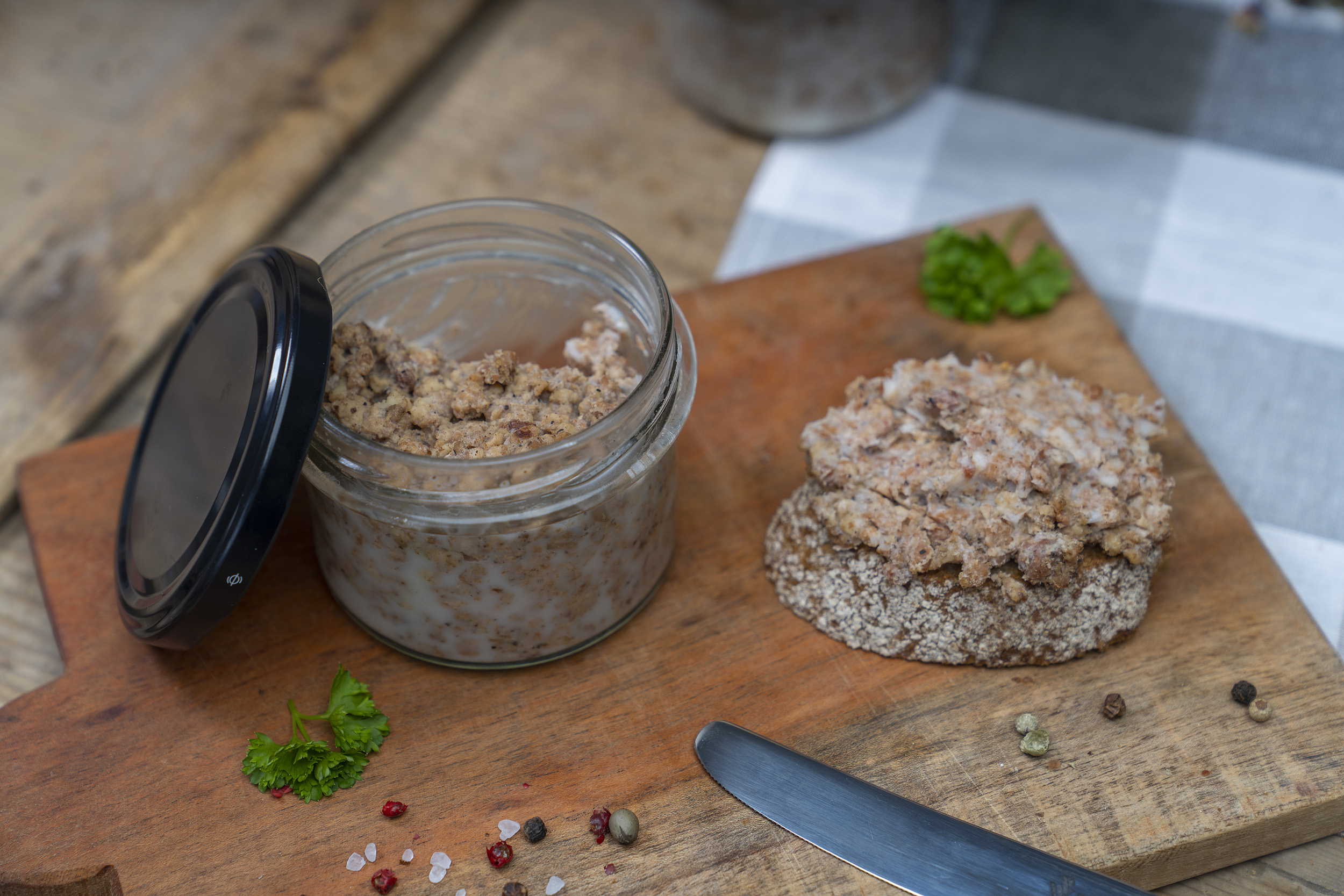Auf einem Holzbrett ein Glas Pott Suse, also geschmortes Hackfleisch. Daneben eine Scheibe Brot mit Pott Suse und Gewürze.