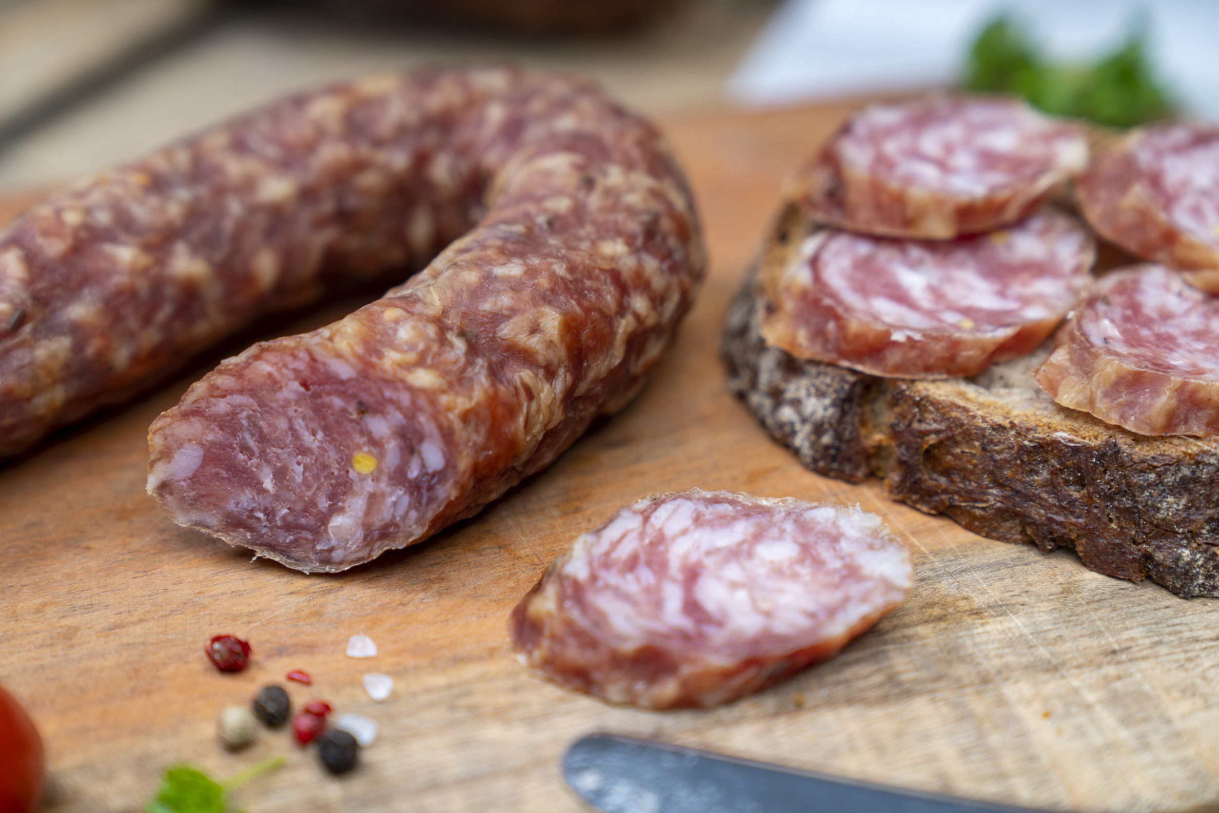 Ein Südharzer Knüppelchen auf einem Brett. Daneben ein Brot mit der Wurst und Gewürze.
