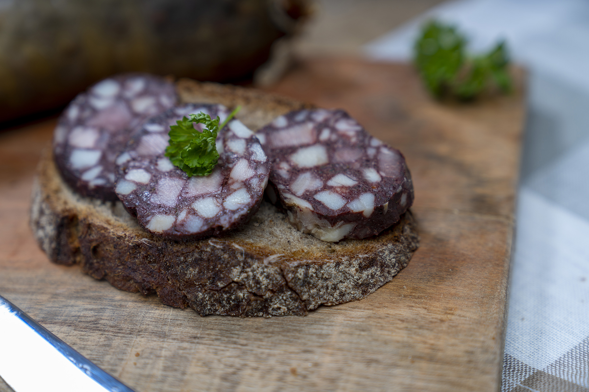 Eine Scheibe Brot mit Rotwurst Scheiben. Auf dem Brett Kräuter und die Wurst.