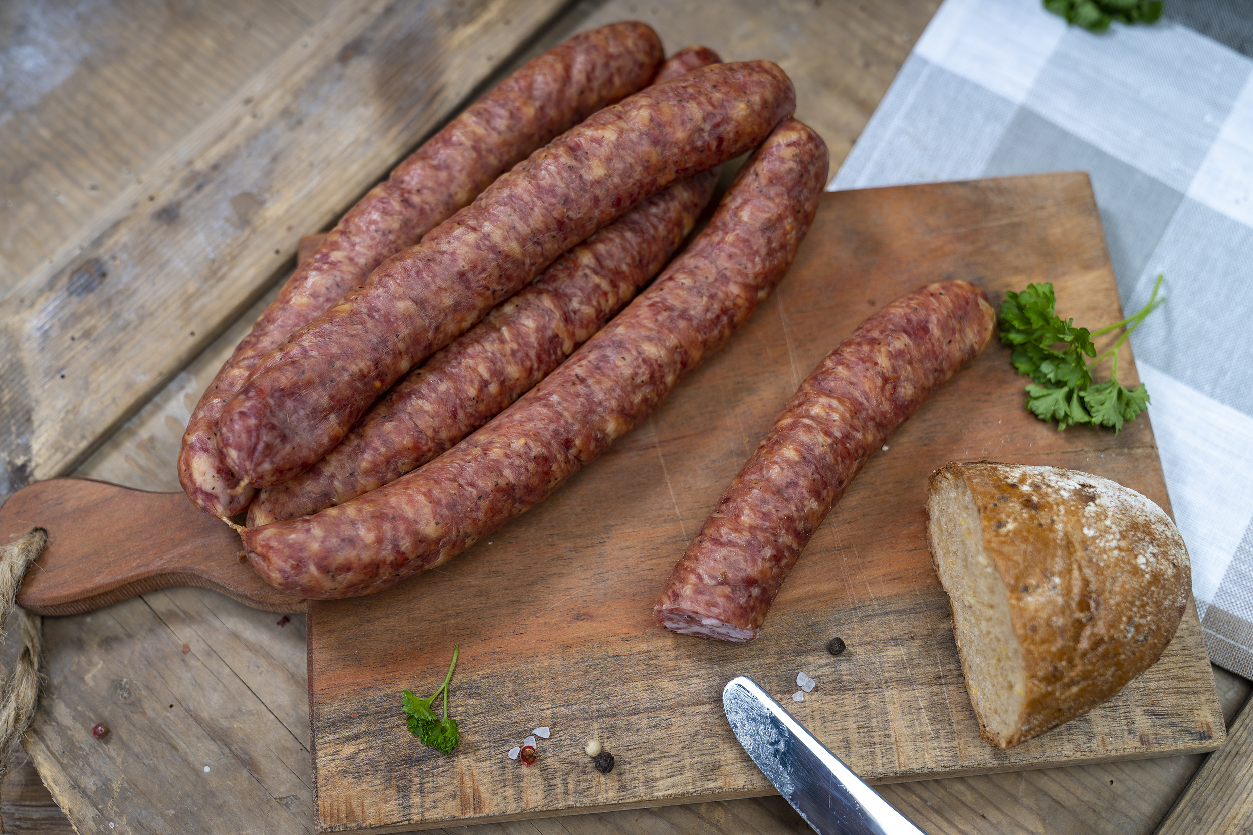 Einige Knacker auf einem Holzbrett. Daneben ein Brot und Gewürze.