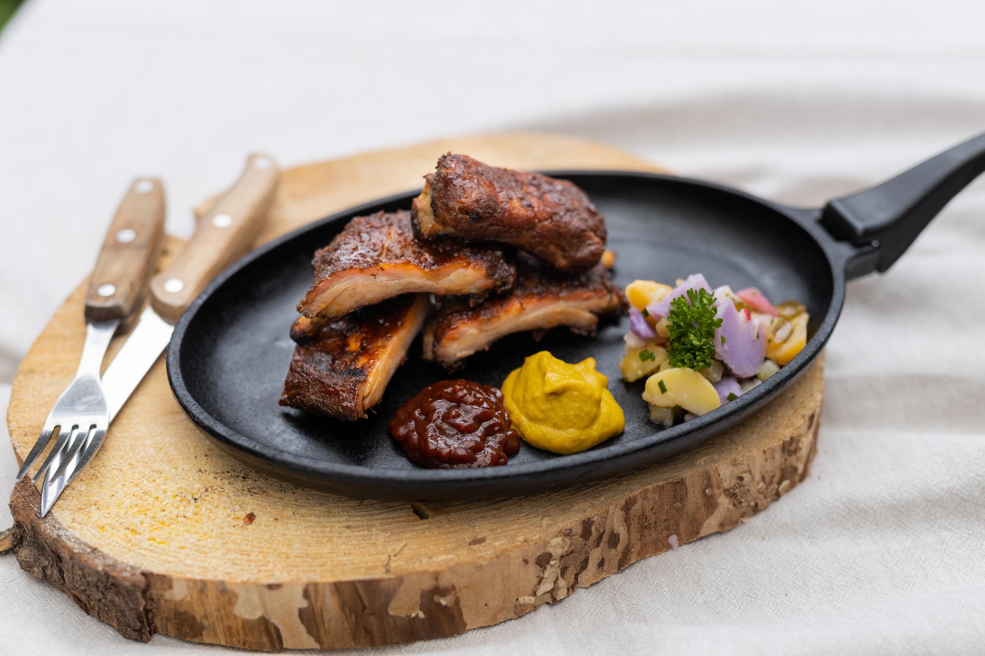 Spare Ribs in einer Pfanne auf einem Brett. MIt verschiedenen Saucen und Salatbeilage.