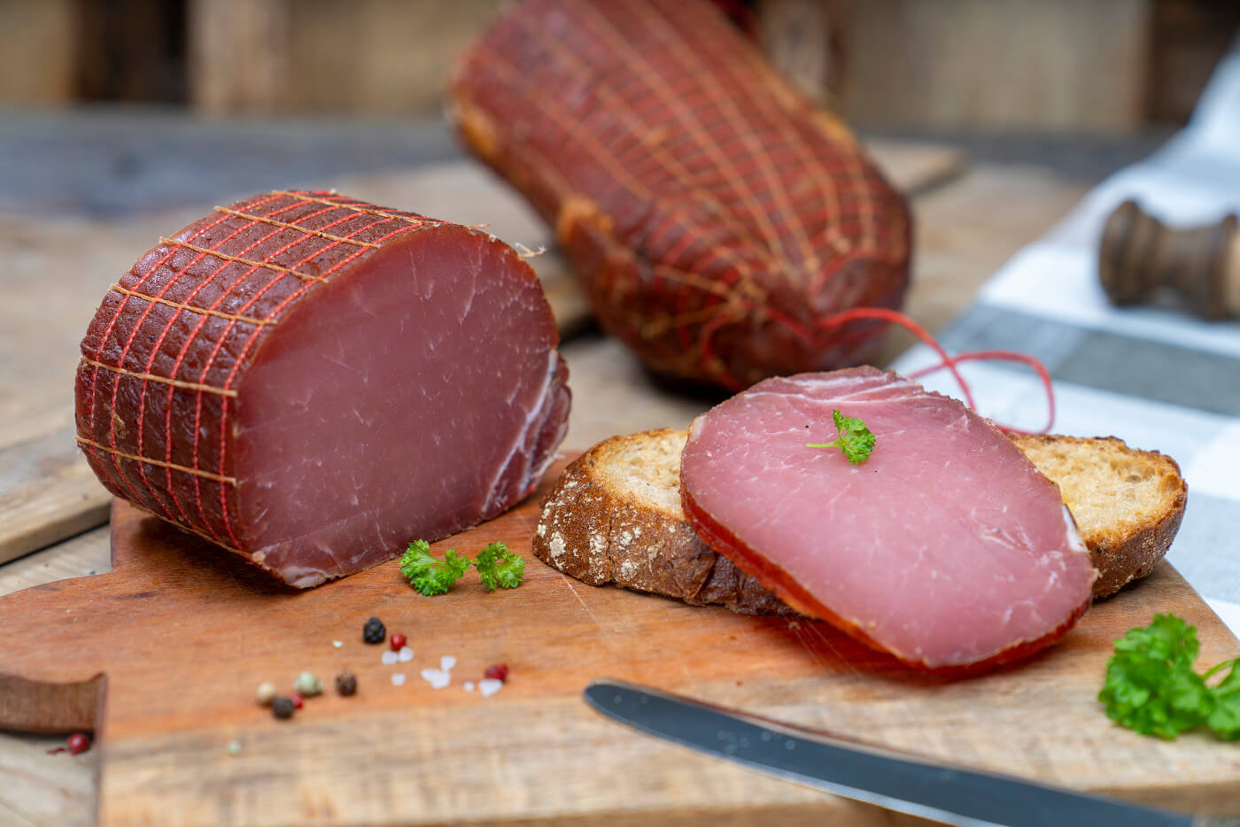 Auf einem Brot eine Scheibe Lachsschinken. Daneben Petersilie und der Schinken. Hinten ein weiterer Schinken.