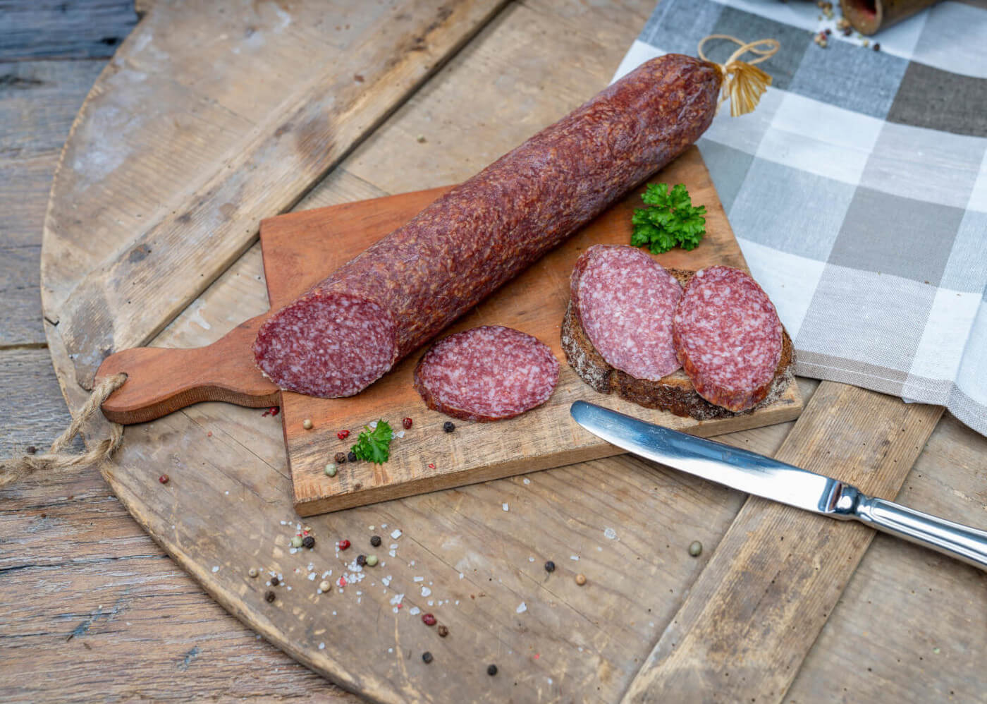 Eine Bauernsalami auf einem Brett. Daneben ein paar Scheiben der Wurst und Brot.