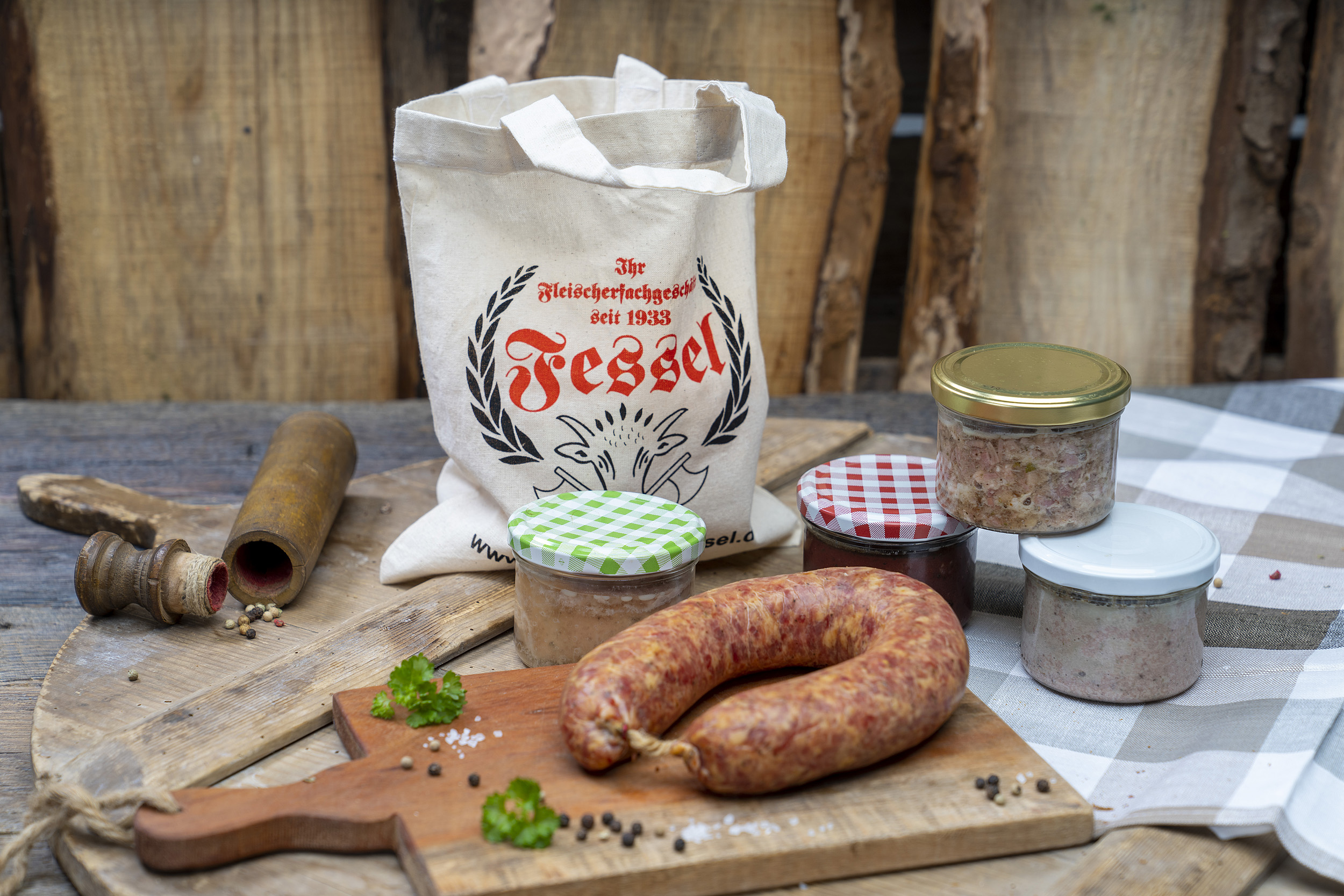 Eine Knackwurst und verschiedene Gläser auf einem Tisch. Dahinter ein Jutebeutel der Fleischerei Fessel für den Fresssack.