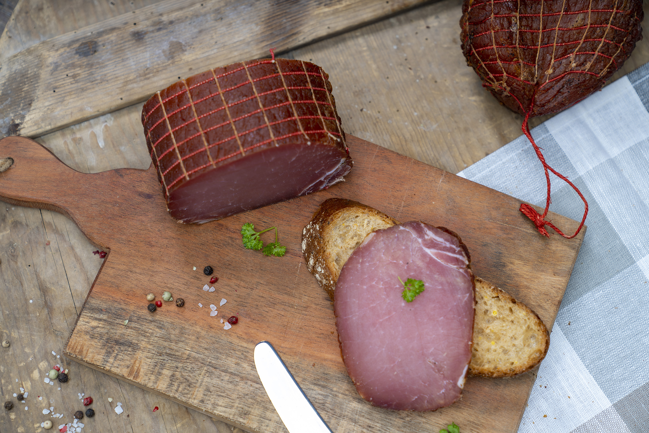 Auf einem Brot eine Scheibe Lachsschinken. Daneben Petersilie und der Schinken. Daneben ein weiterer Schinken.