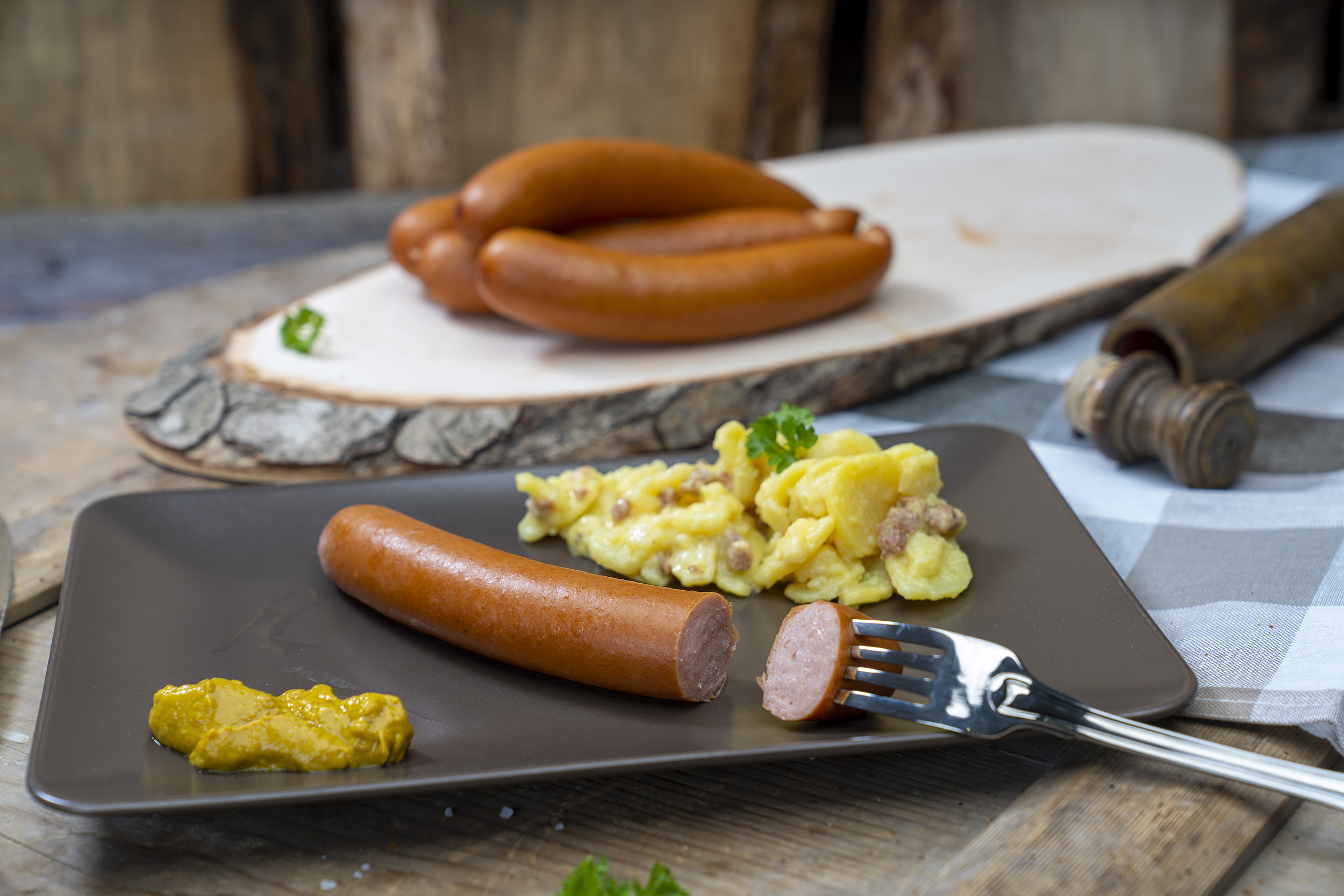 Bockwurst auf einem Teller mit Senf und Kartoffelsalat. Hinten mehr Bockwürsten der Fleischerei Fessel.