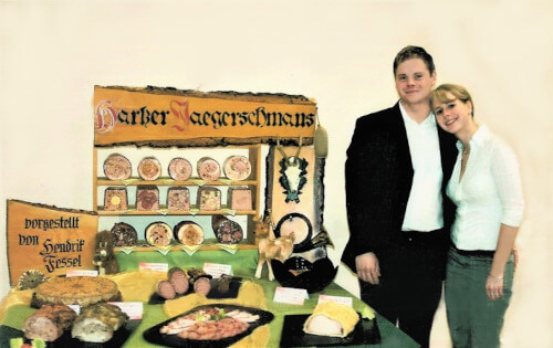 Hendrik und Olga Fessel vor seinem Meisterstück. Auf einem Tisch liegen viele Fleischspezialitäten unter der Überschrift Harzer Jaegerschmaus.